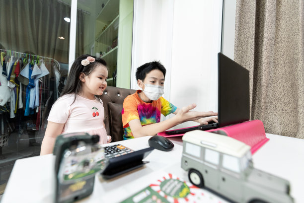 一个亚洲可爱的男孩在家里学习在线课程，与他的妹妹社交距离，隔离和自我隔离。图片下载