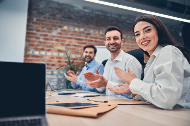 快乐的队友们坐在办公桌前拿着笔记本电脑图片下载