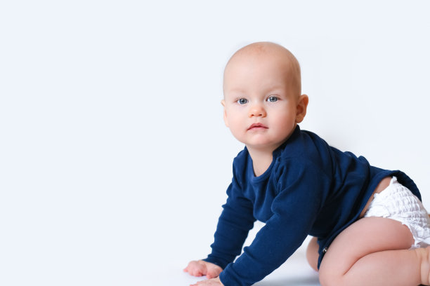 婴儿在蓝色的衬衫和尿布的copyspace文字爬行在地板上的白色工作室背景。一个白人小孩看着镜头图片下载