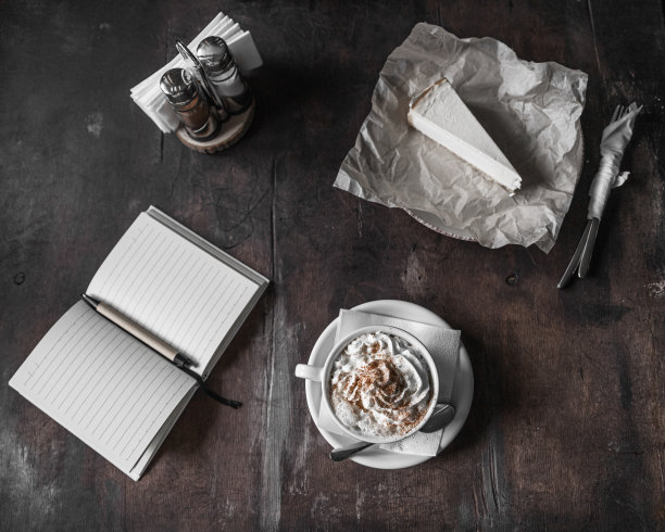 黑暗的照片。卡布奇诺加生奶油旁边是笔记本和芝士蛋糕。舒适的咖啡店，选择性的专注图片下载
