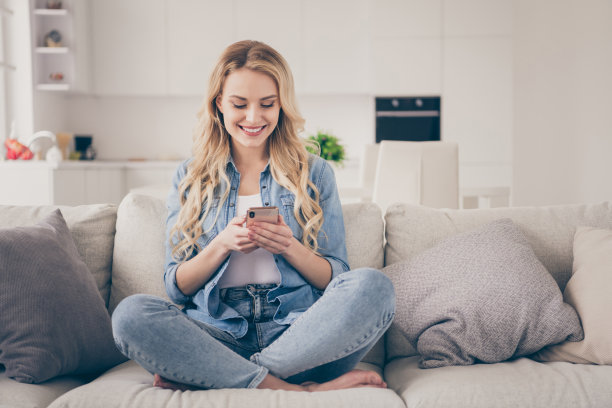 迷人的金发女士的照片坐在舒适的沙发双腿交叉呆在家里保持电话浏览网站自由职业者远距离工作隔离时间客厅室内图片下载