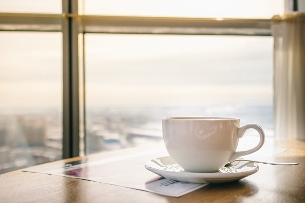 白色的杯子和一杯热饮在一个餐厅的桌子上，与早晨的城市全景图片下载