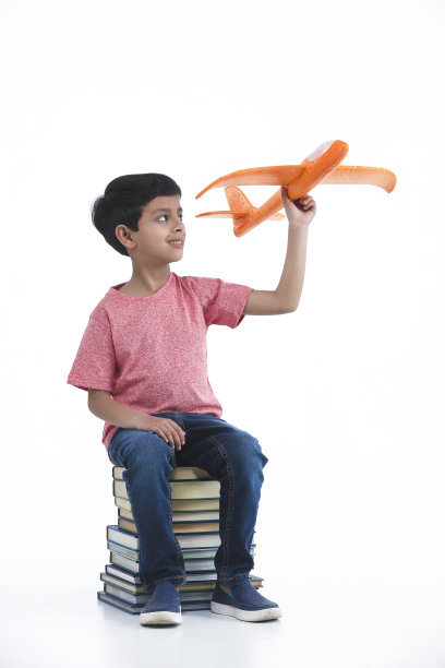 孩子坐在书本上玩飞机模型图片下载