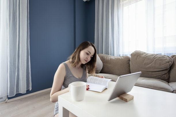一名年轻的女学生坐在她公寓的地板上，手里拿着数字平板电脑图片下载