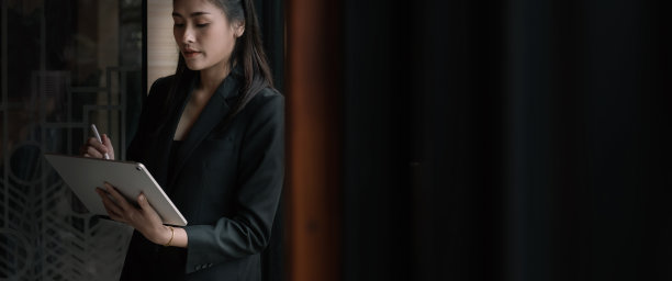 有魅力的亚洲商务女性站在办公大楼窗前使用电子平板电脑图片下载