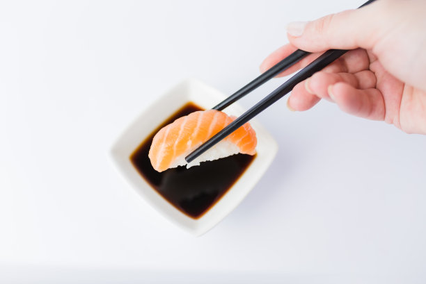 女性用筷子将美味的三文鱼手握寿司放入碗中，酱油放在白色的背景上。副本的空间。图片下载