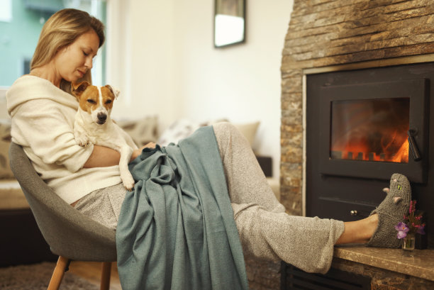 舒适的山间周末，女人在舒适的家里穿着放松靠近壁炉，拥抱狗图片下载