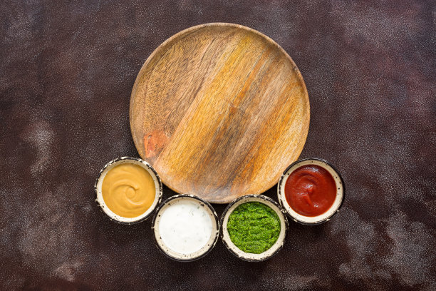 空木盘和各种酱料的框架在一个黑暗的乡村背景。酱料:西红柿，芥末，香蒜沙司和奶油与绿色。俯视图，平放。图片下载