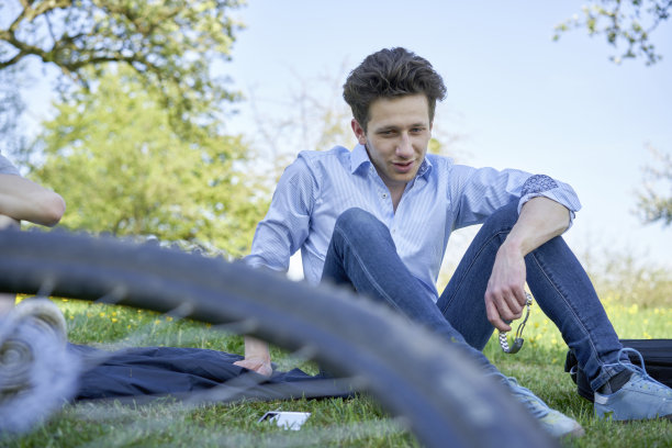年轻的男子坐在草坪上，在美丽的绿色自行车旅行图片下载
