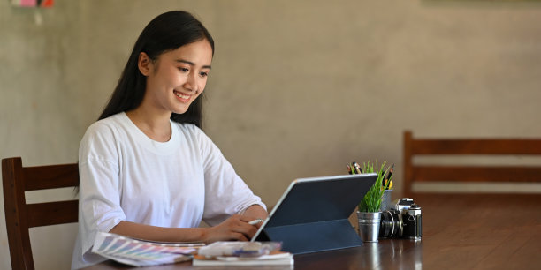 这张照片是一位创意女性坐在老式客厅水泥墙的木制办公桌前，用手写笔在平板电脑上写字的照片。图片下载