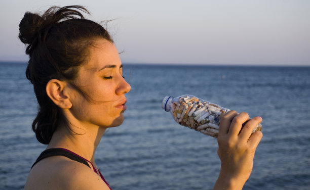 喝了一整瓶香烟的女人。寓意照片特写，关注水和环境污染的原因，没有吸烟成瘾。环境污染概念照片。图片下载