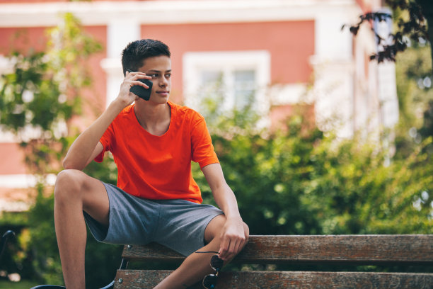 一个青少年正坐在公园的长椅上打手机图片下载