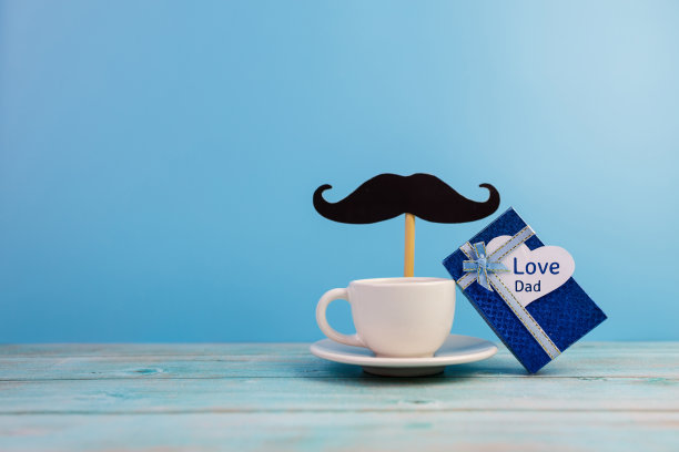 父亲节理念快乐。一张黑色的小胡子纸，一杯咖啡和在一张白色的心纸上写着“爱爸爸”的文字。图片下载