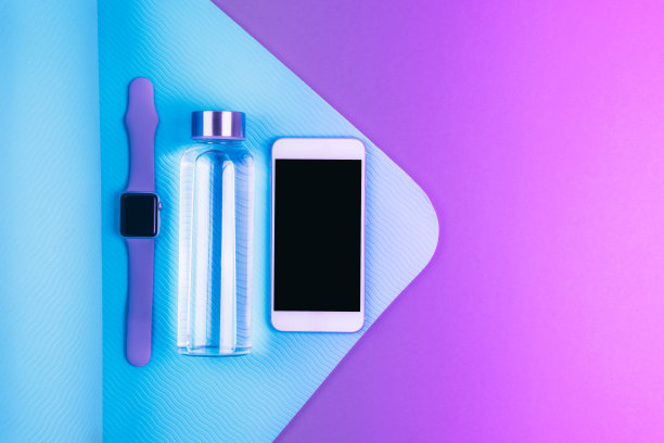 俯视图可重复使用的生态玻璃水瓶，智能手机和跟踪手表在绿松石蓝色纹理瑜伽垫上霓虹灯紫色的背景与文本的地方图片下载