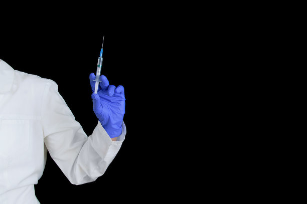 护士戴着外科防护蓝手套，拿着注射器，在黑色的背景上打针。图片下载