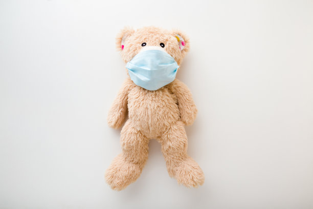 棕色泰迪熊，口鼻面罩，浅灰色桌子背景。第一次保护在危险的病毒时期。儿童医疗保健的概念。关闭了。自顶向下的观点。图片下载
