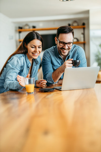 幸福随意的情侣坐在桌边喝着咖啡和果汁，看着笔记本电脑，画像。图片下载