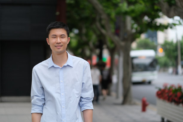 街上一幅穿着衬衫的亚洲年轻人对着镜头微笑的照片。图片下载
