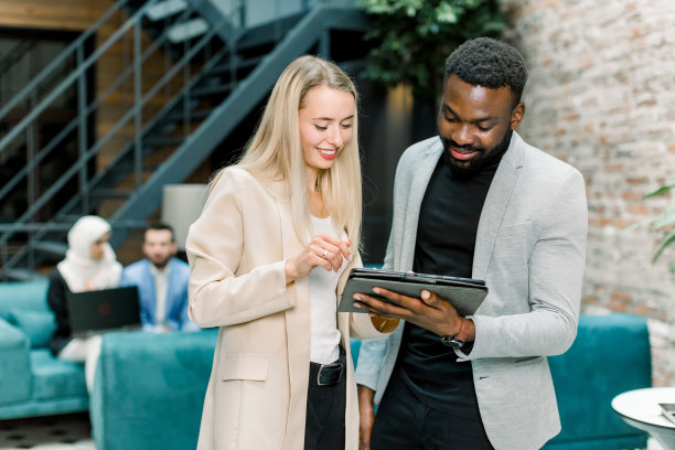 正面图片是成功微笑的年轻多种族商人，白人妇女和非洲胡子男子，站在办公室里互相交谈，看着平板电脑图片下载