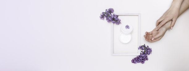 美丽的女性手与丁香花和一个白色的木制框架在白色的背景，俯视图。护手霜在镜框里。护肤理念，水疗。横幅图片下载