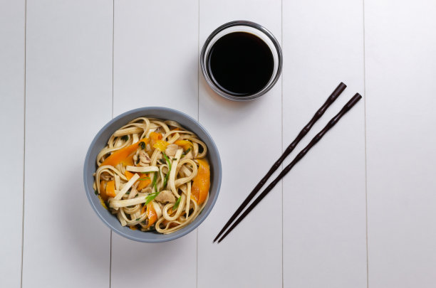 乌冬面配鸡肉、酱油和竹竿，放在白色盘子里。前视图。日本料理。图片下载