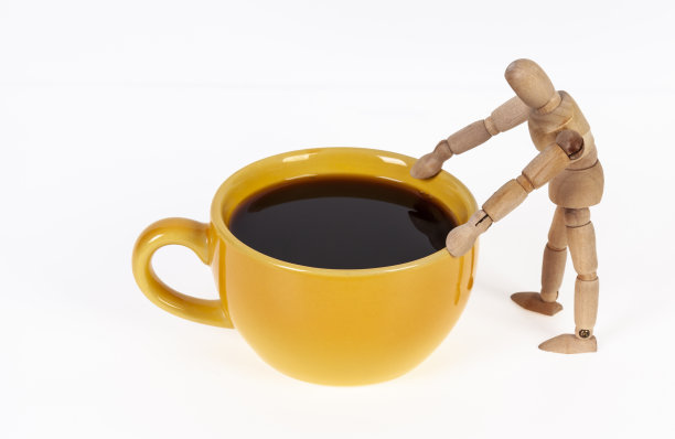 一个木头人站在一杯黑咖啡旁边。图片下载