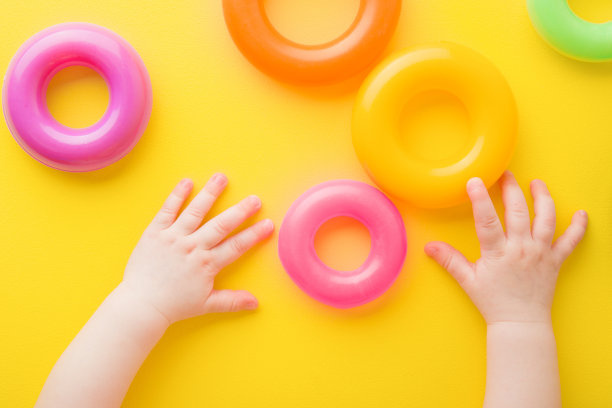宝宝的手在亮黄色的桌子上玩着五颜六色的塑料戒指。特写镜头。给小孩子的发展玩具。视角拍摄。自顶向下的观点。图片下载