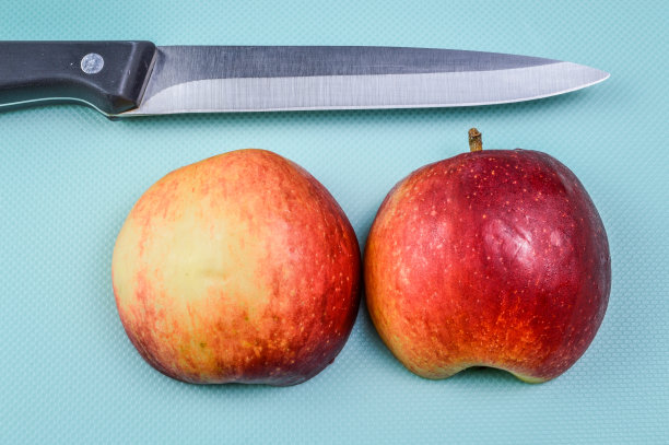 两个半红苹果和一把菜刀在浅蓝色纹理的背景上靠近图片下载