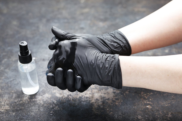 双手戴黑色防护手套，用防病毒液消毒。素材图片