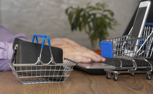 购物车。在后台，一名男子在一台笔记本电脑上订购一件产品。有选择性的重点。在线购物。图片下载