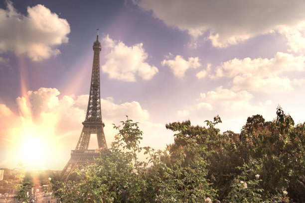 透过夏日的绿树和夕阳的余晖俯瞰埃菲尔铁塔。美丽浪漫的背景。法国巴黎战神广场的埃菲尔铁塔图片下载