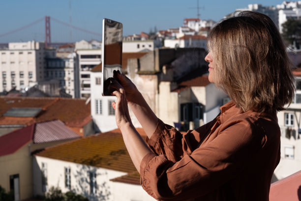一位黑头发的妇女站在自家阳台上的写字板上拍摄黎明的照片，从那里可以看到旧城的景色图片下载