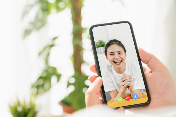 年轻微笑的亚洲女子在网上视频通话，从家里用智能手机与朋友交谈。图片下载