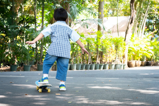 一个小男孩站在公园的滑板上。背面。图片下载