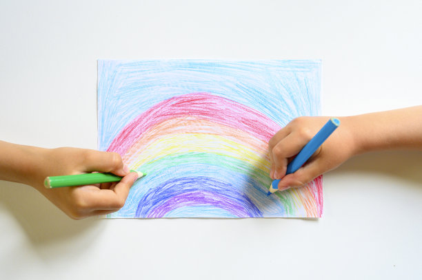 小朋友双手一起在白色的背景上画彩虹色的铅笔图片下载