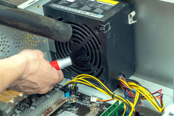 维修及清洁电脑设备。一个特写的服务人员清除灰尘和污垢从一个电脑电源风扇与刷子和真空吸尘器。图片下载