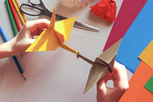 孩子们的手在白色的背景上用黄色的纸做折纸鹤。一步一步的折纸教程。孩子的创意观念，回到学校。图片下载