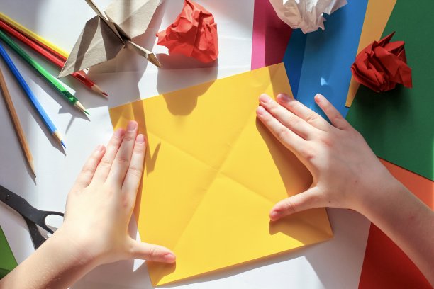 孩子们的手在白色的背景上用黄色的纸做折纸鹤。一步一步的折纸教程。孩子的创意观念，回到学校。图片下载