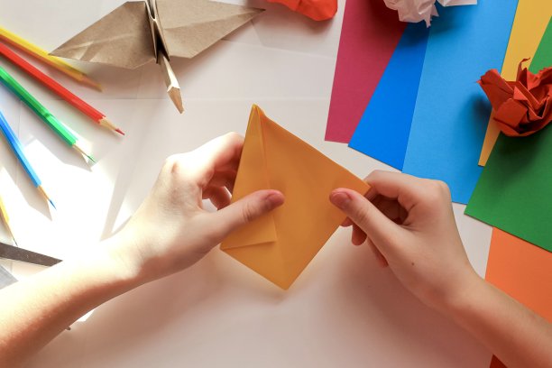 孩子们的手在白色的背景上用黄色的纸做折纸鹤。一步一步的折纸教程。孩子的创意观念，回到学校。图片下载