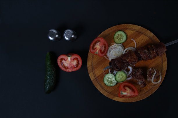 将切好的蔬菜放在木砧板上，盐和胡椒瓶放在黑色的背景上平铺图片下载