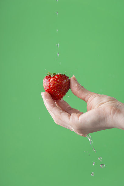 女人的手在绿色饱和的背景上洗草莓。图片下载