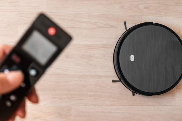 人的手拿着一个遥控器，打开吸尘器机器人来打扫公寓。智能家居，无线技术概念图片下载