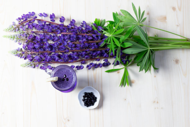 平铺在一张有复印空间的木桌上，上面放着一杯新鲜的香蕉、蓝莓奶昔和紫色的羽扇豆花图片下载