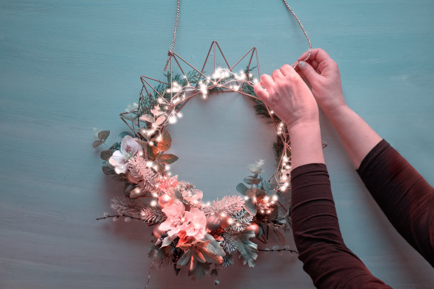 用圣诞花环装饰门。女性的手把绳子固定在金属底座上手工制作的花环上，圣诞装饰品和冬季植物的色调图片。图片下载