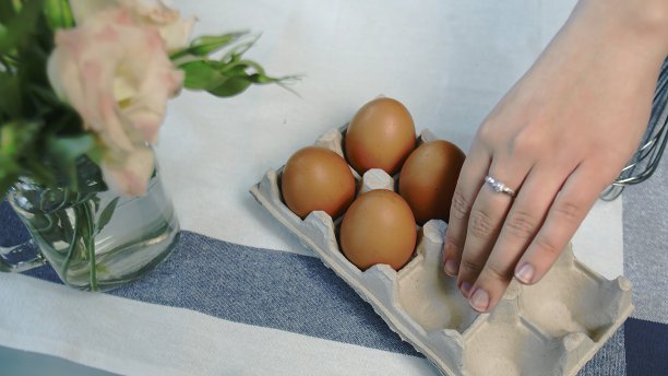 鸡蛋装在纸板箱里放在桌子前面，一个家庭主妇拿着一个。图片下载
