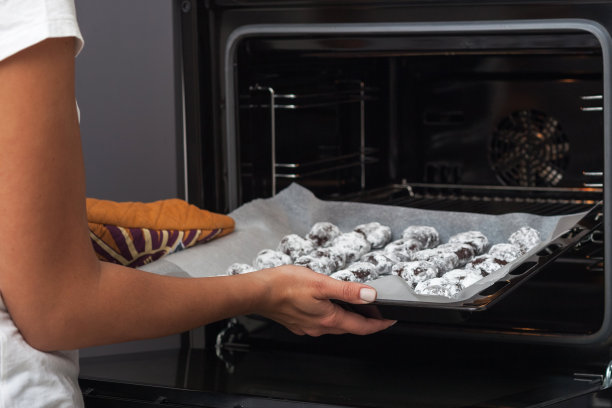 制作布朗尼饼干的过程。照片中是女性的双手，正在把饼干放进烤箱。图片下载