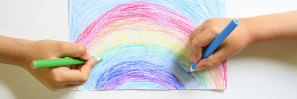 小朋友双手一起在白色的背景上画彩虹色的铅笔。横幅图片下载