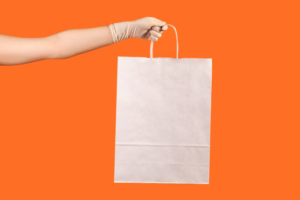 侧面特写的人的手在白色的外科手套拿着和显示白色的购物袋。图片下载