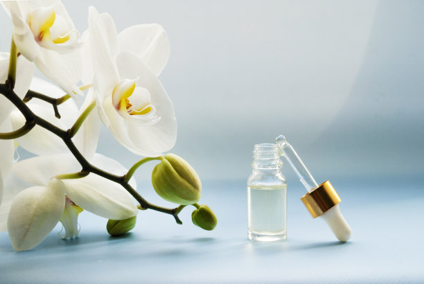 化妆品精油，带滴管的透明瓶子，白色兰花，浅蓝色背景，护肤素材图片