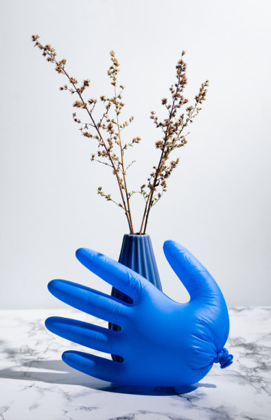 极简主义的照片，深蓝色花瓶与干燥的植物和乳胶手套在大理石表面上的灯光背景图片下载